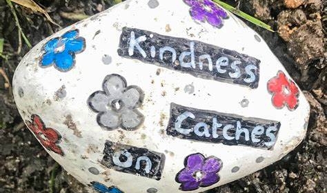A stone decorated in paint with flowers and the words 'kindness catches on' written on it
