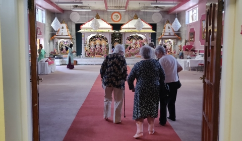 Photograph of three older people walking into a Hindu temple