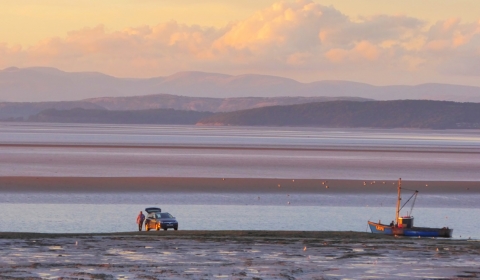 Photo of Morecambe bay sands down to the sea with a couple of small fishing boats and views out to the Lake District fells behind