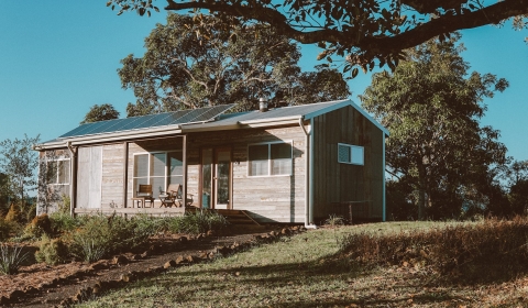 A house made of wood on a hill under a tree with solar panels on the roof in Australia