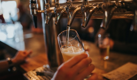 A photograph of a hand that is holding a glass and pulling a glass of beer.