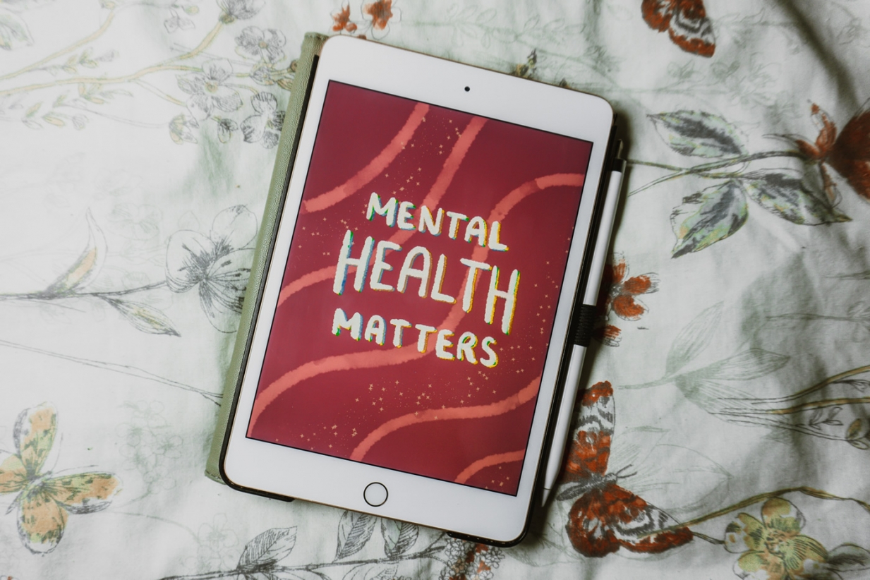 A flat lay image of tablet device on a floral fabric background. The tablet screen displays the text 'Mental health matters' in a white script font.