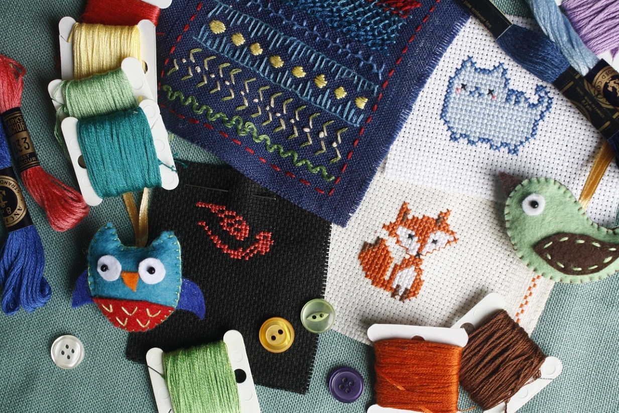 An assortment of textile craft items and materials such as buttons and threads. there is cute cross stitch fox and cat as well as felt birds.