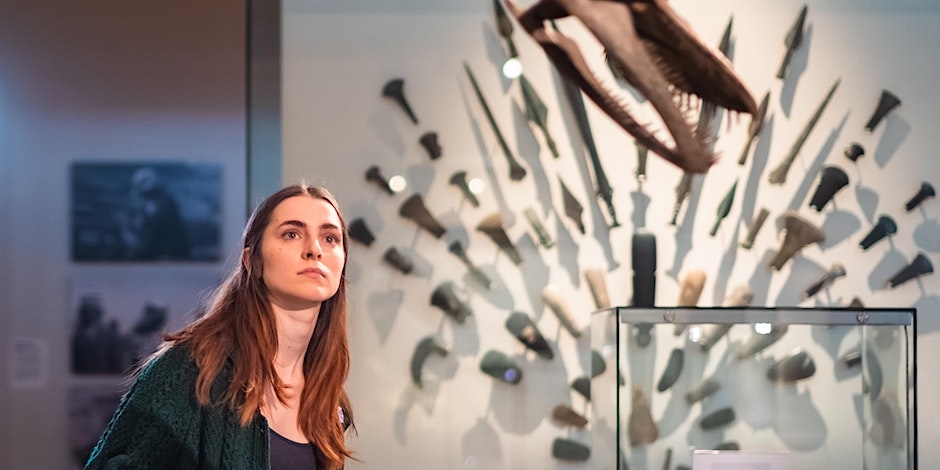A women in a museum looking in the distance behind her a series of different historical artefacts.