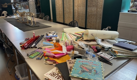 Photograph depicting art materials and books on a table, in a museum setting.