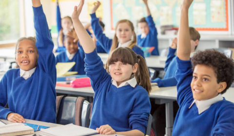 happy children in a classroom raising their hands as if to answer questions