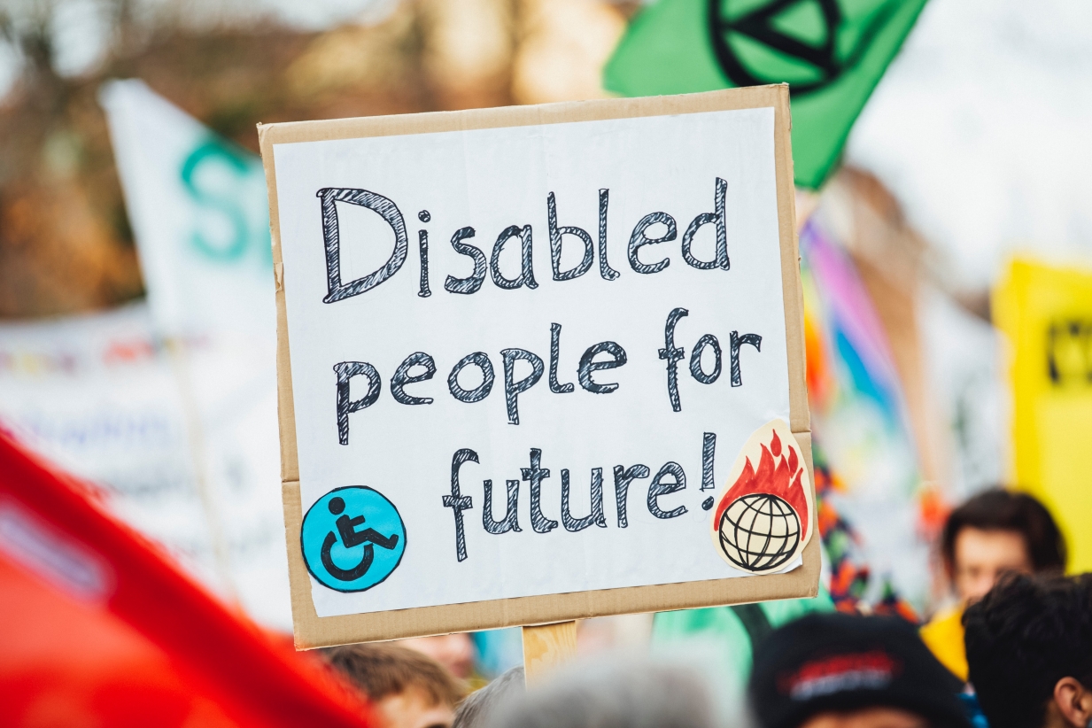 A hand holds up a placard with 'Disabled people for future' written by hand on it
