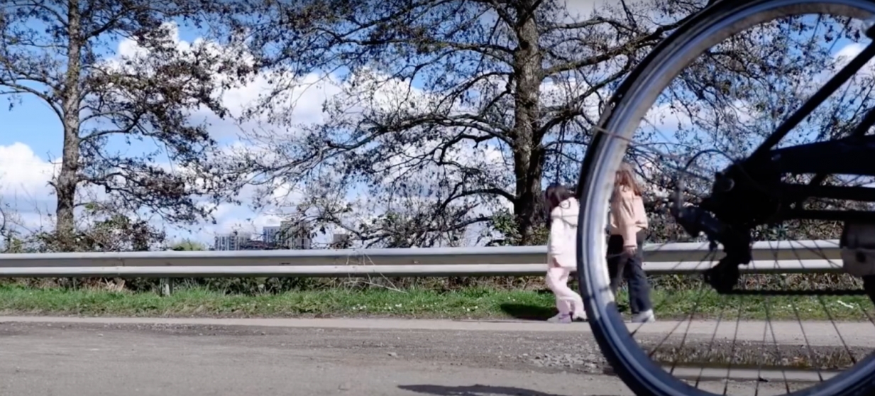 Photograph of a bike wheel riding past a girl and woman walking.