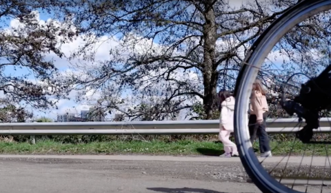 Photograph of a bike wheel riding past a girl and woman walking.
