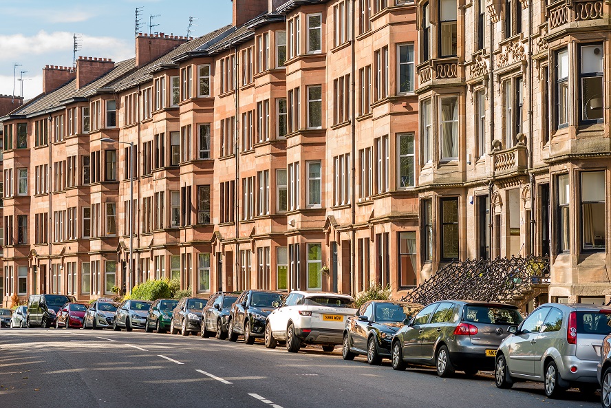 A row of tenement buildings with cars parked outside the houses.